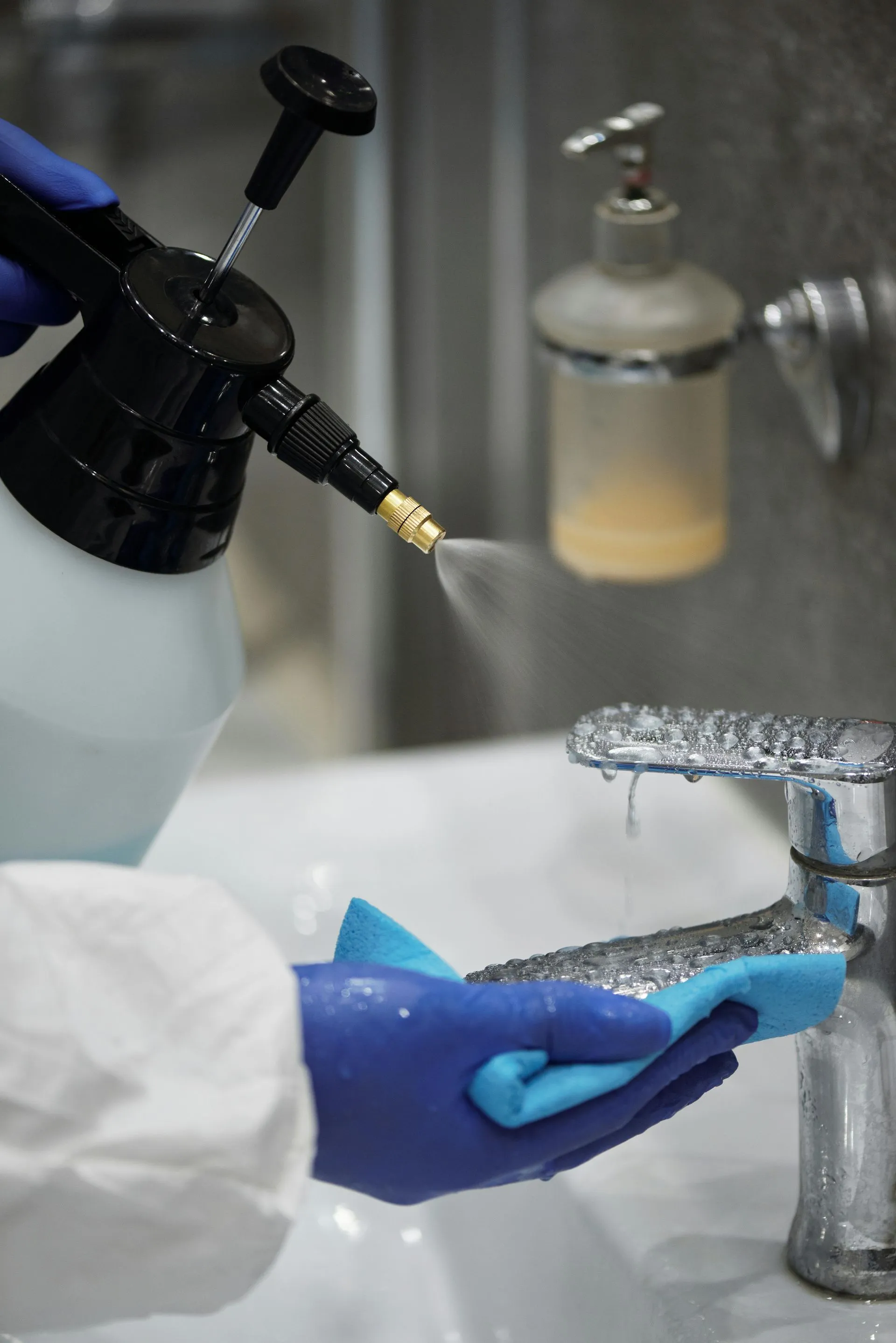 A person is cleaning a sink with a spray bottle and a sponge.