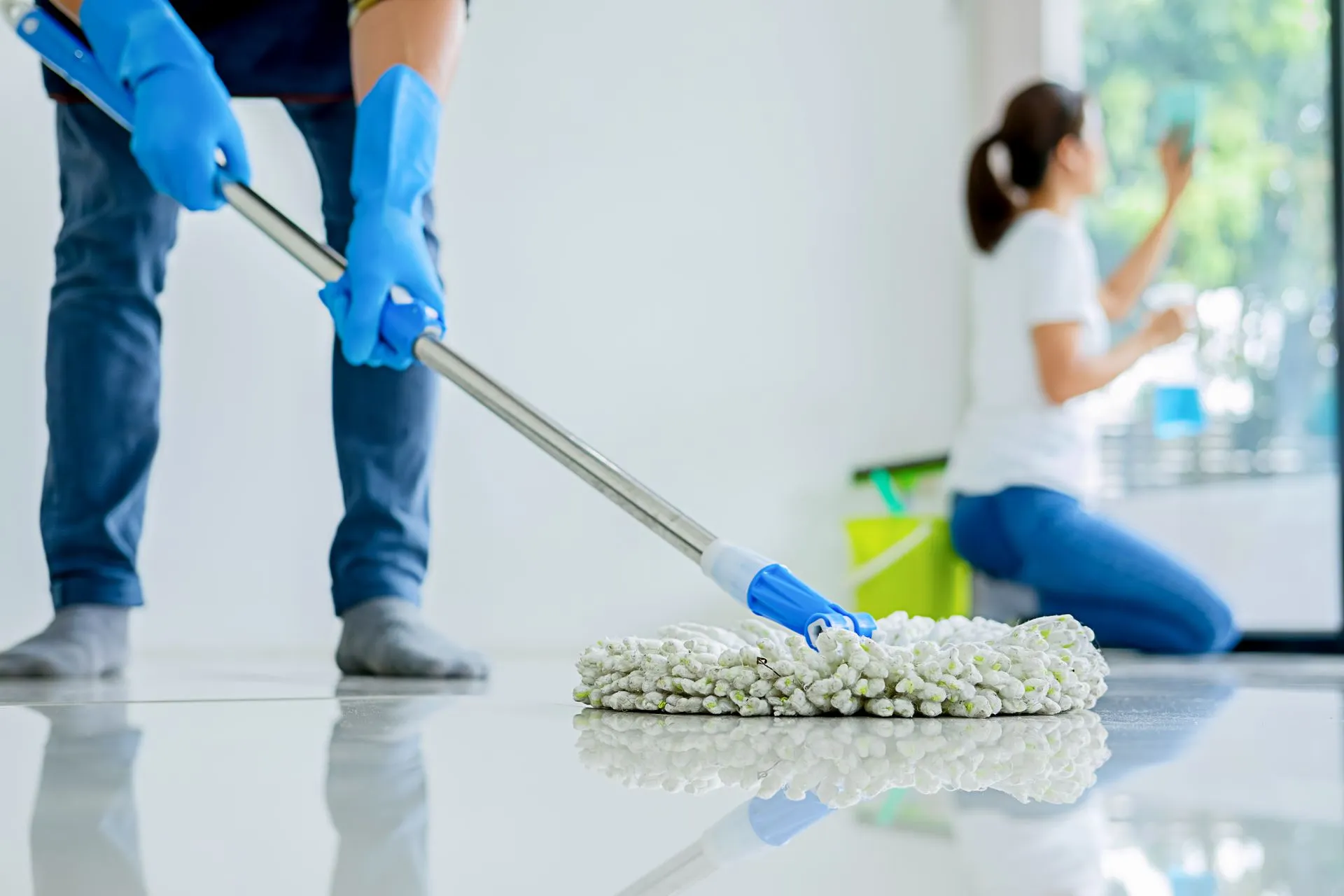 A man is mopping the floor while a woman is cleaning the window.