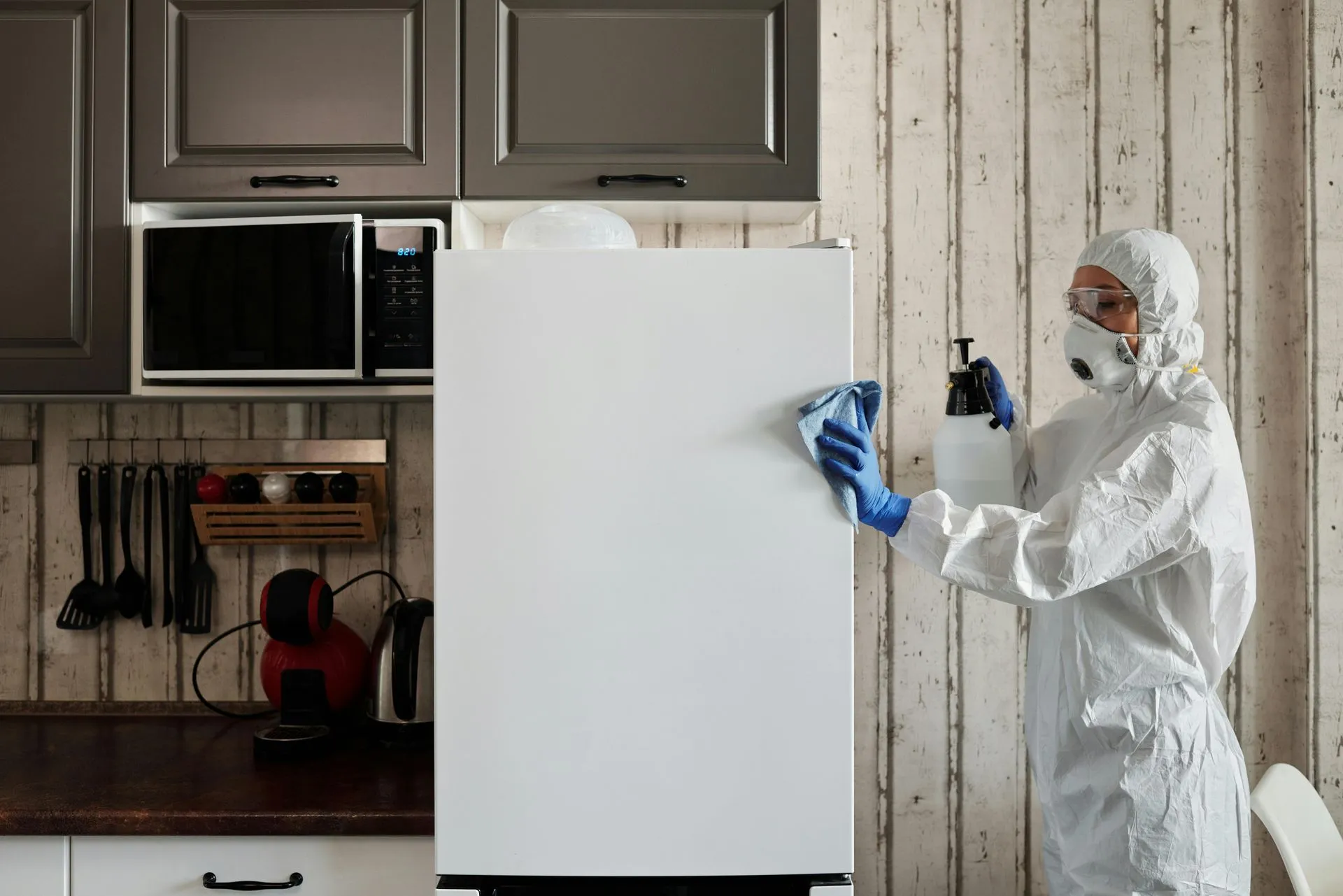 A man in a protective suit is cleaning a refrigerator in a kitchen.