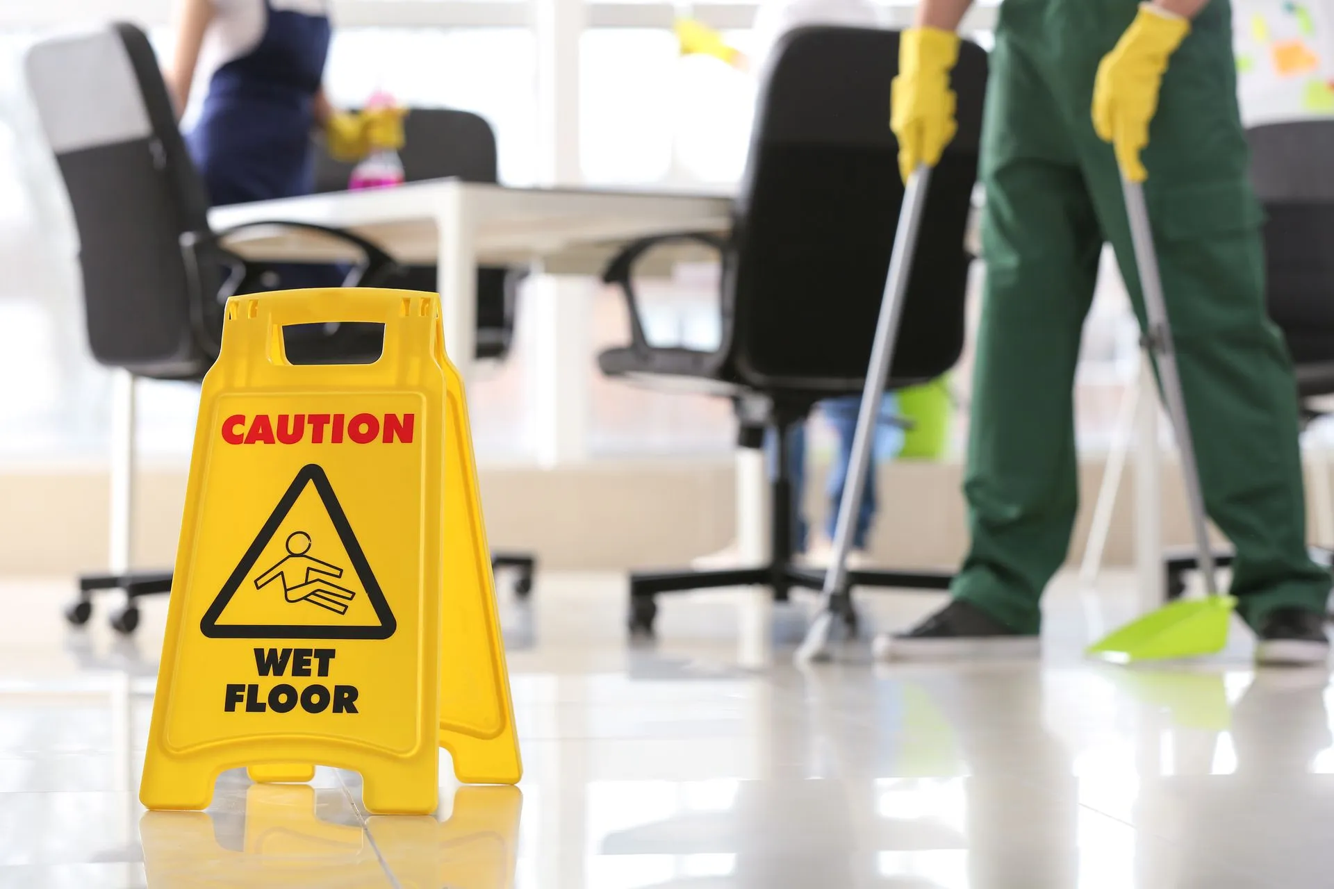 A man is mopping the floor in an office next to a caution wet floor sign.
