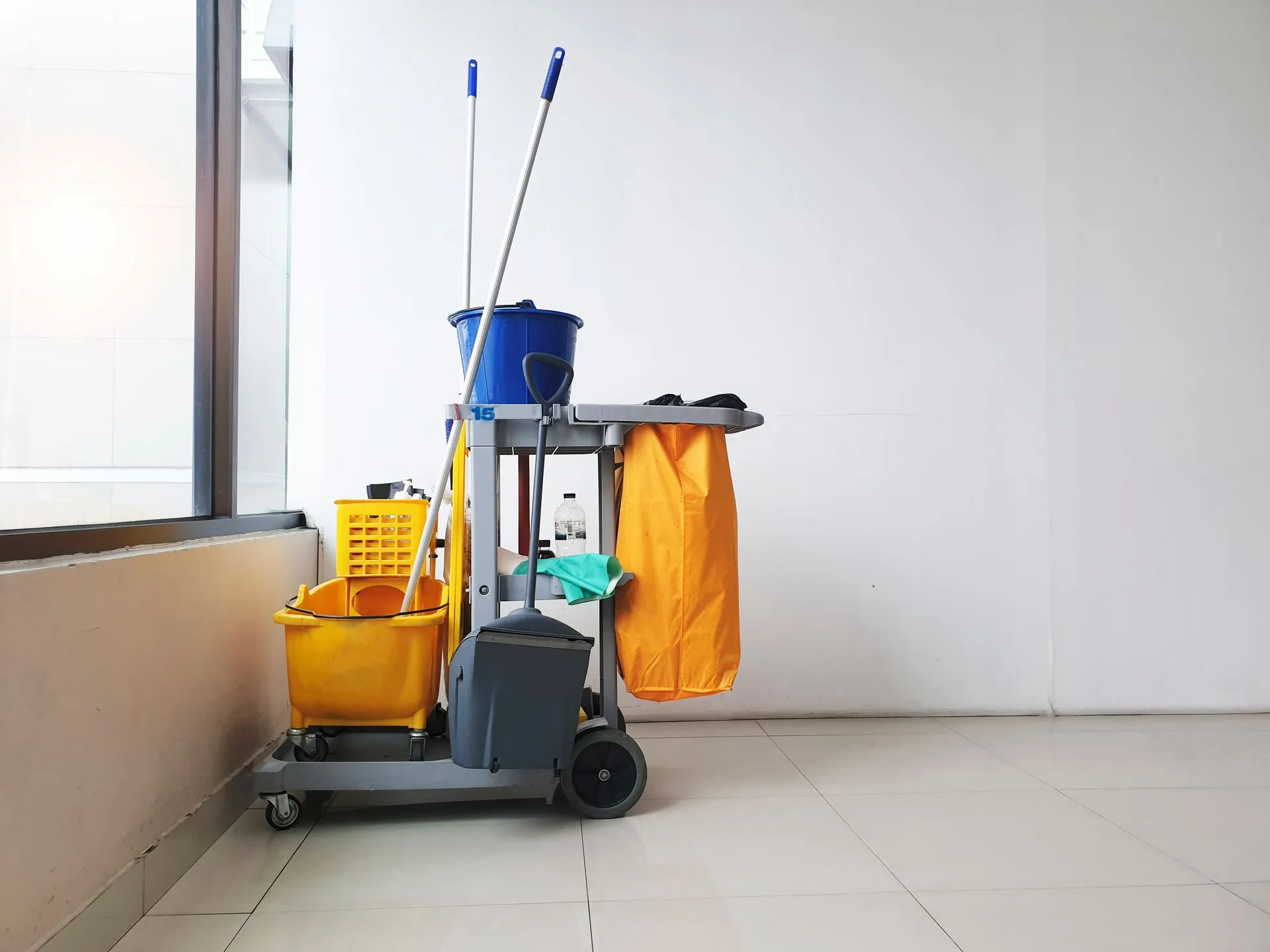 A cleaning cart with mop , bucket , and gloves in an empty room.