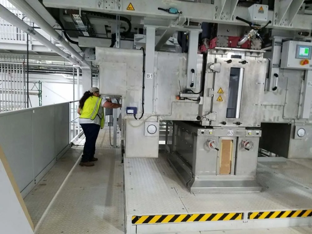 A man in a yellow vest is working on a machine in a factory.