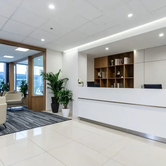 Bright modern office lobby with white reception desk, potted plant, seating area, and large windows